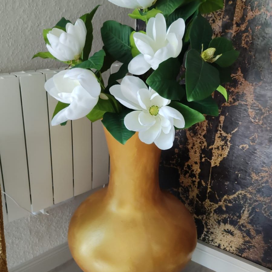 Goldene Vase mit weißen Magnolienblüten und grünen Blättern.