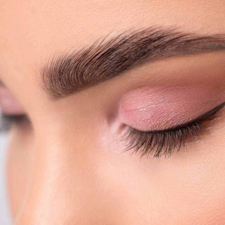 Nahaufnahme eines geschlossenen Auges mit zartem Lidschatten und betonten Wimpern.