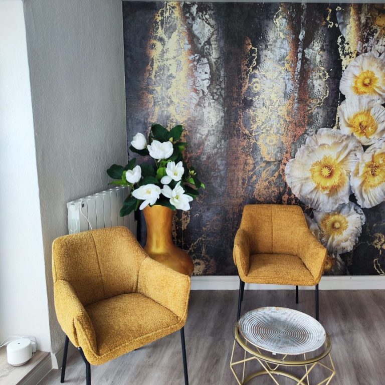 Zwei senfgelbe Stühle vor einer Wand mit Blumenmuster und einer Vase mit Blumen.